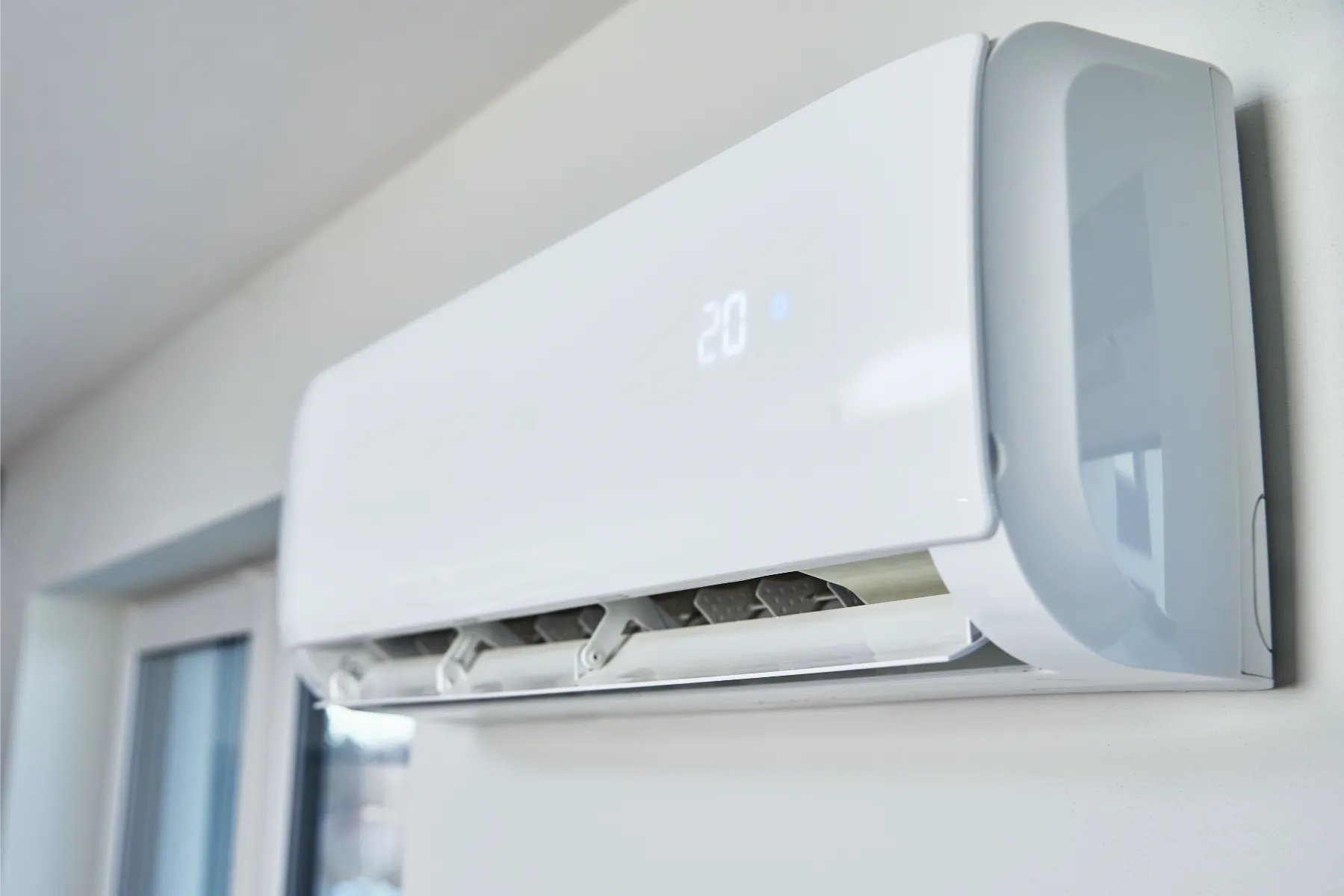 Biały klimatyzator ścienny zainstalowany na ścianie, wyświetlający temperaturę 20°C