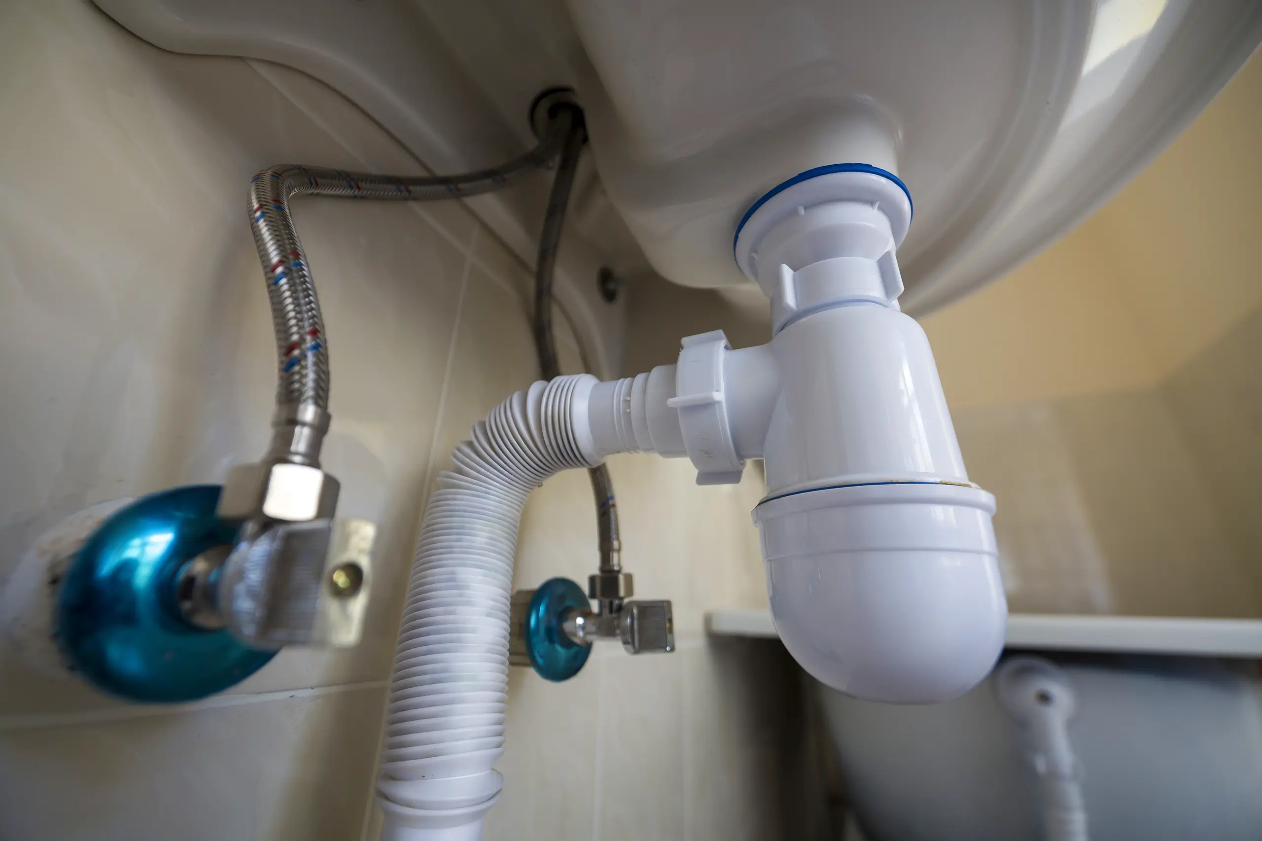 Zbliżenie na instalację hydrauliczną umieszczoną pod umywalką, ukazujące syfon oraz przyłącza wody