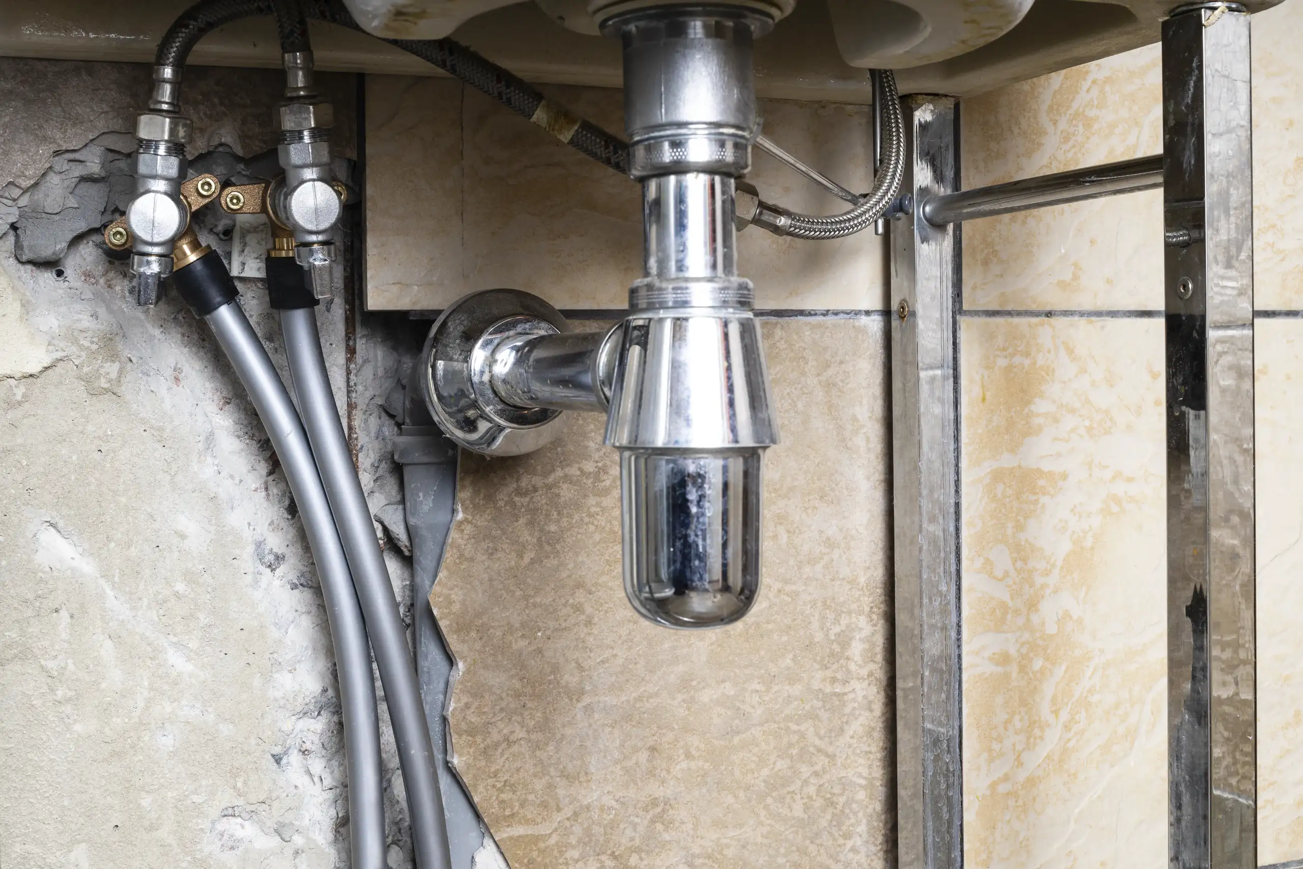 Instalacja hydrauliczna pod zlewem, widoczne rurki i armatura, przygotowanie do montażu